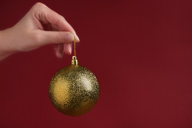 Woman holding golden Christmas ball on red background, closeup. Space for text