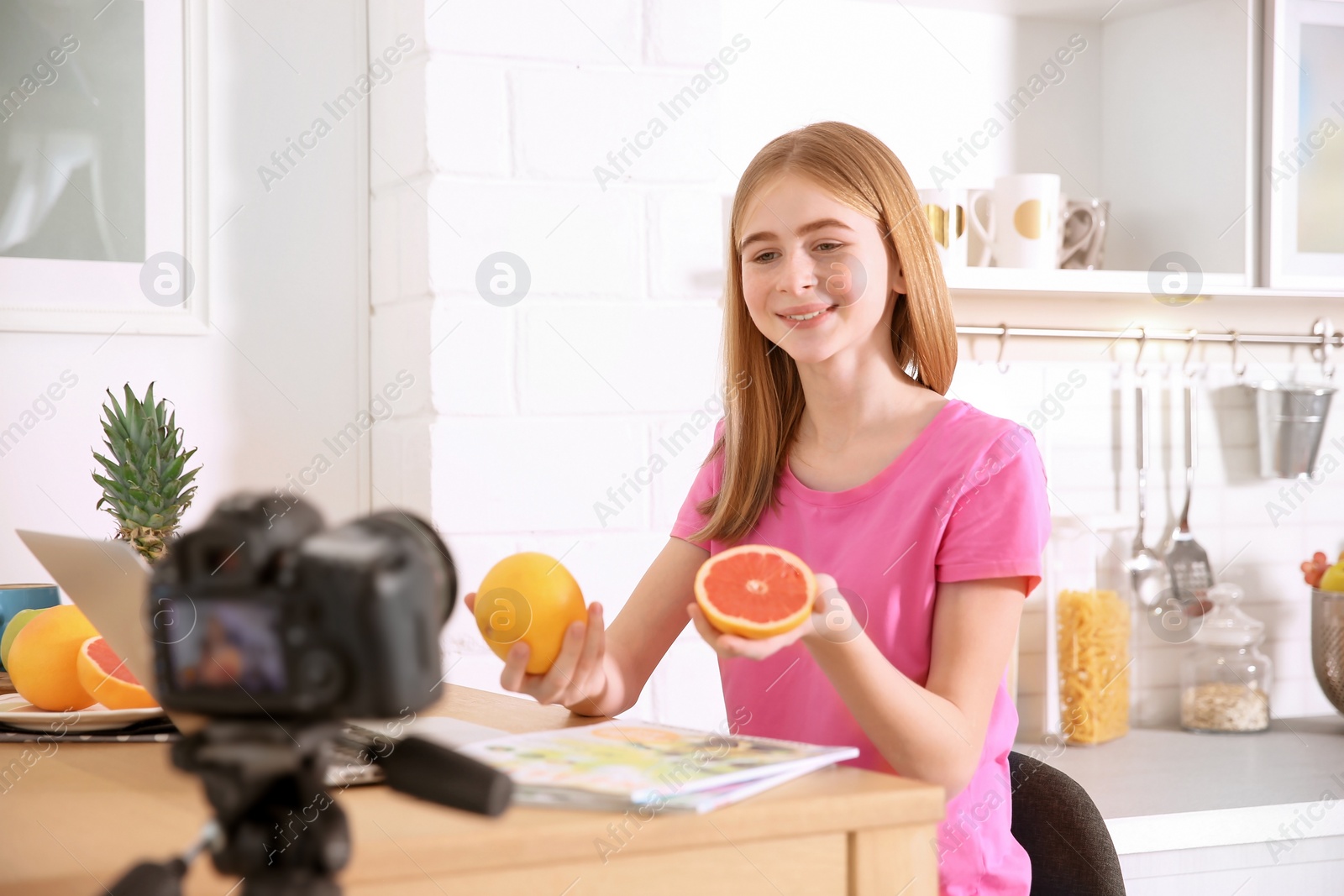 Photo of Cute teenage blogger with fruits recording video at table