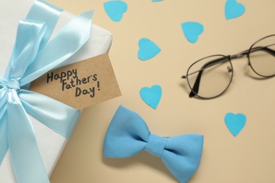 Photo of Card with phrase Happy Father's Day, gift box, paper hearts and men accessories on beige background, top view