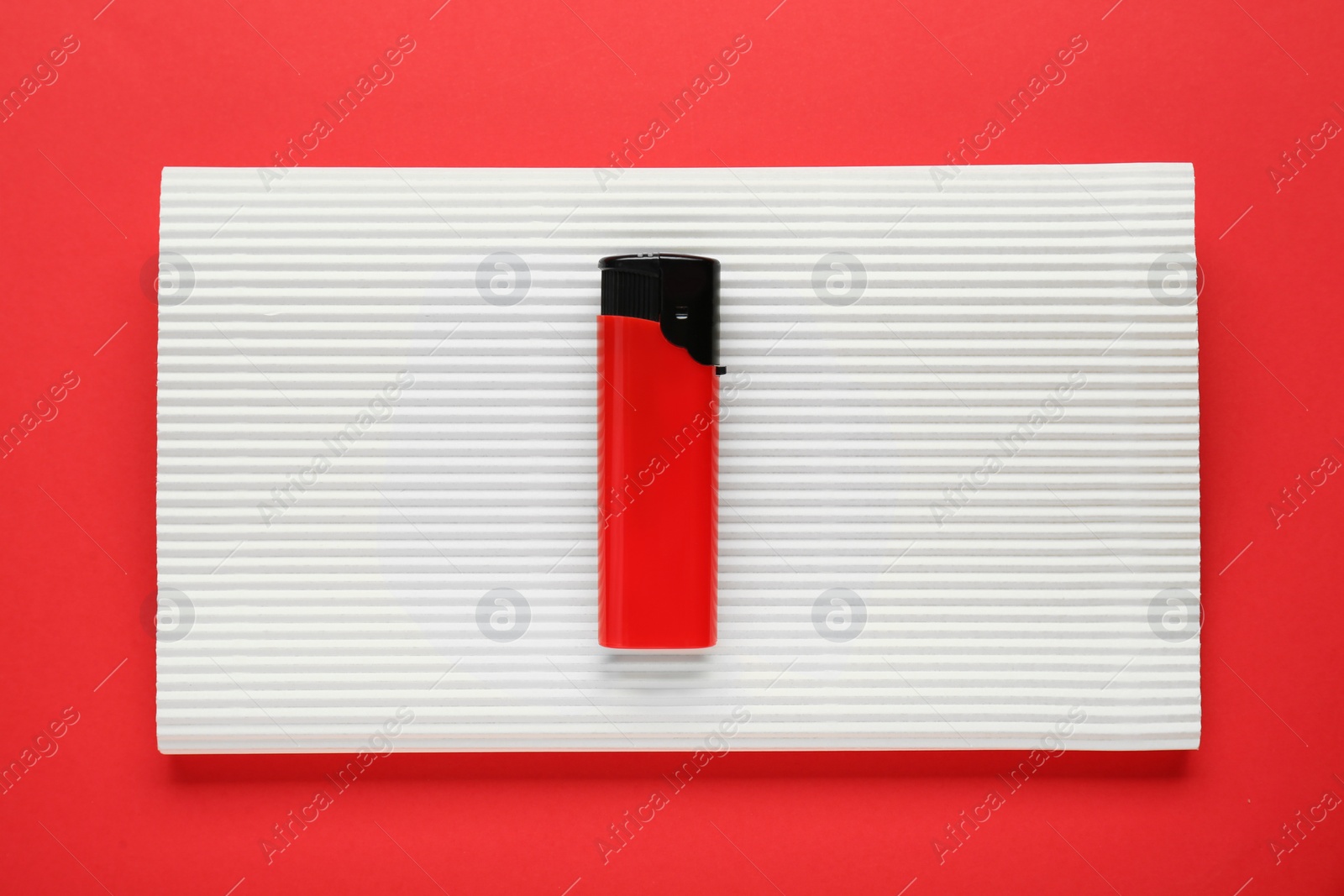 Photo of Stylish small pocket lighter with white corrugated fiberboard on red background, top view