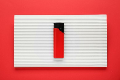 Photo of Stylish small pocket lighter with white corrugated fiberboard on red background, top view