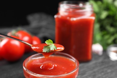 Photo of Taking tasty ketchup with spoon from bowl at table, closeup. Tomato sauce