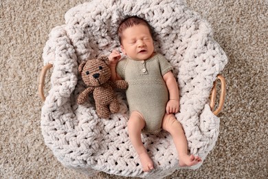 Photo of Cute newborn baby sleeping with toy bear in basket, top view