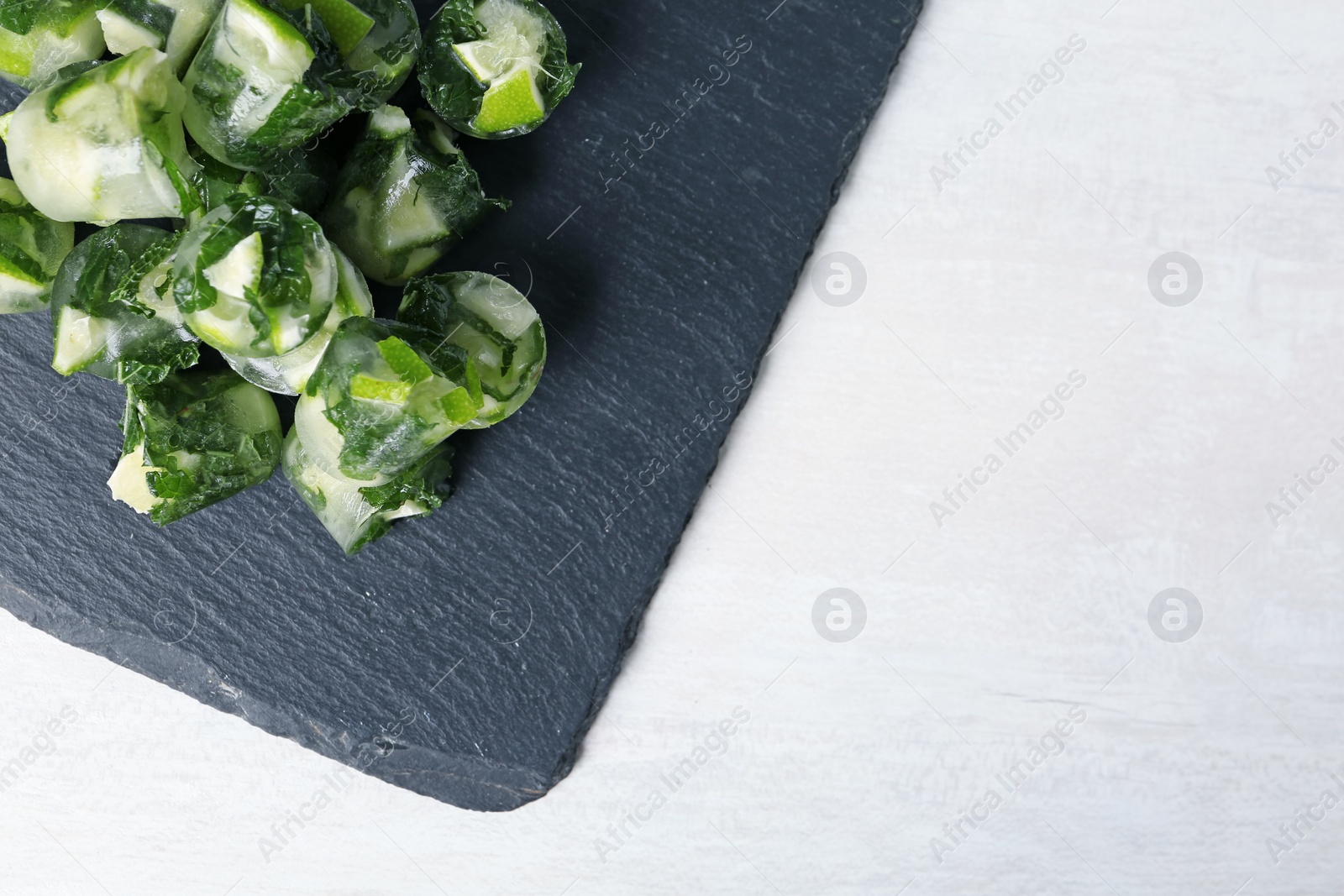 Photo of Slate plate with lime and mint ice cubes on light table, top view. Space for text