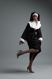 Photo of Woman in nun habit and mesh tights on grey background. Sexy costume