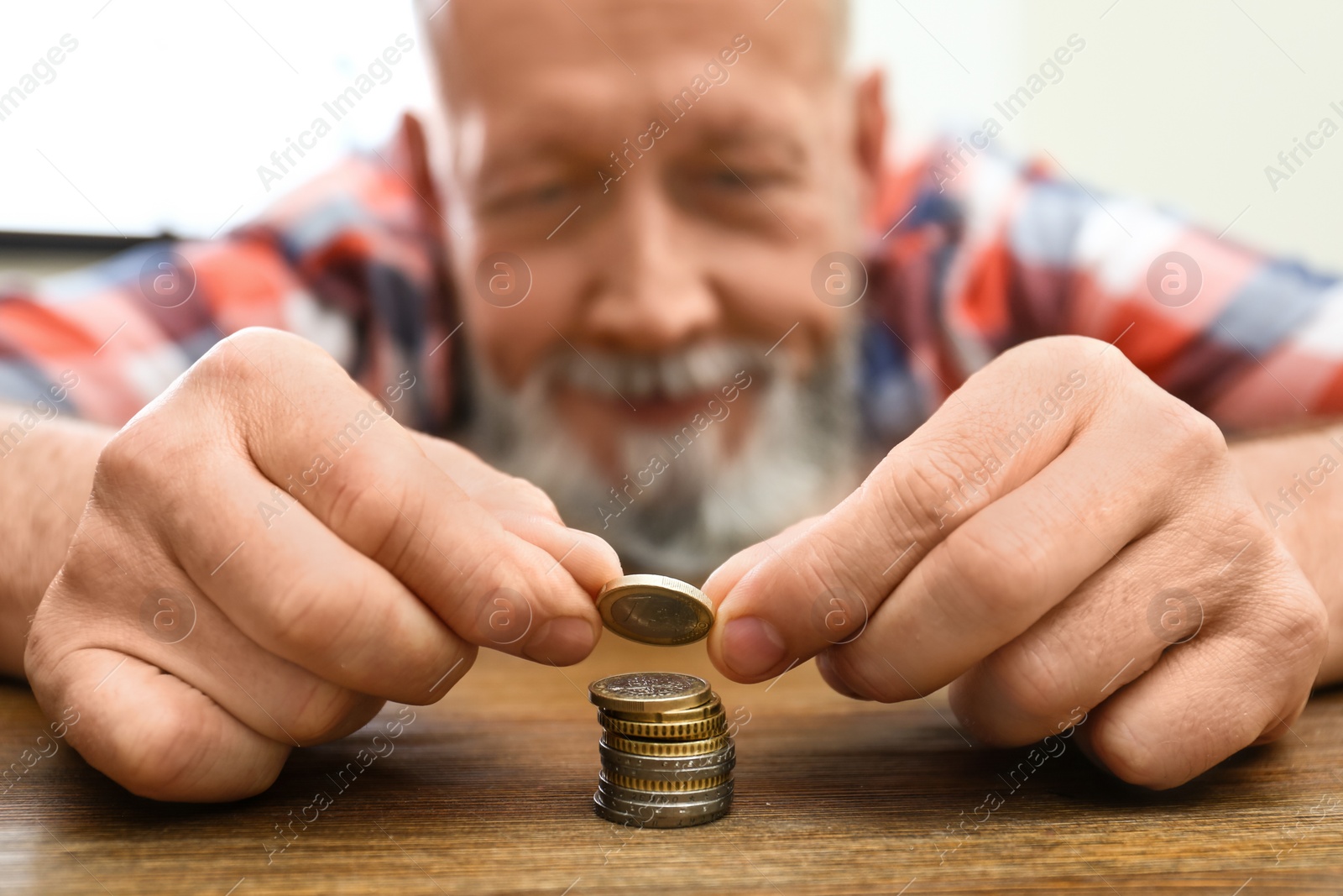 Photo of Senior man stacking up coins at table, focus on hand