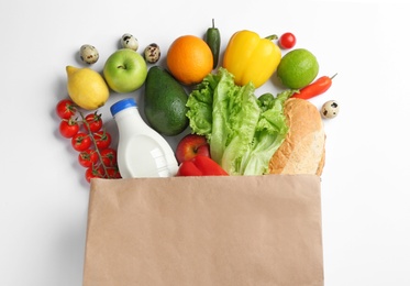 Paper bag with different groceries on white background, top view