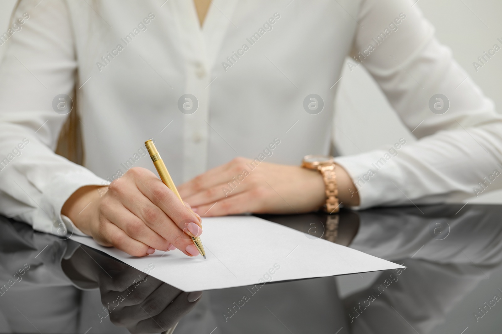 Photo of Woman writing on sheet of paper at glass table, closeup