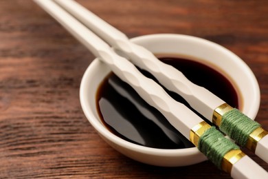 Photo of Bowl with soy sauce and chopsticks on wooden table, closeup