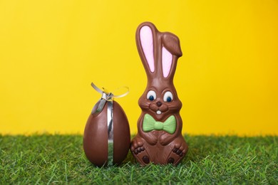 Easter celebration. Cute chocolate bunny and egg on grass against yellow background