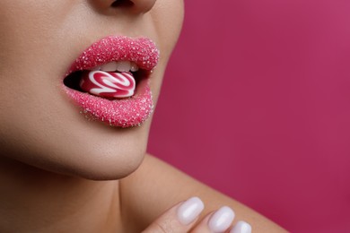 Photo of Woman with lips covered in sugar eating candy on pink background, closeup. Space for text