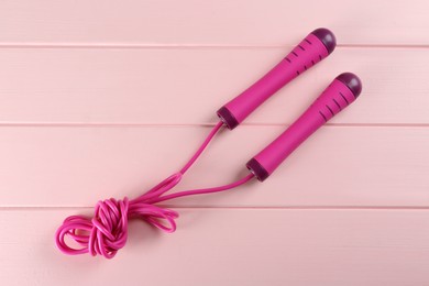 Skipping rope on pink wooden table, top view. Sports equipment