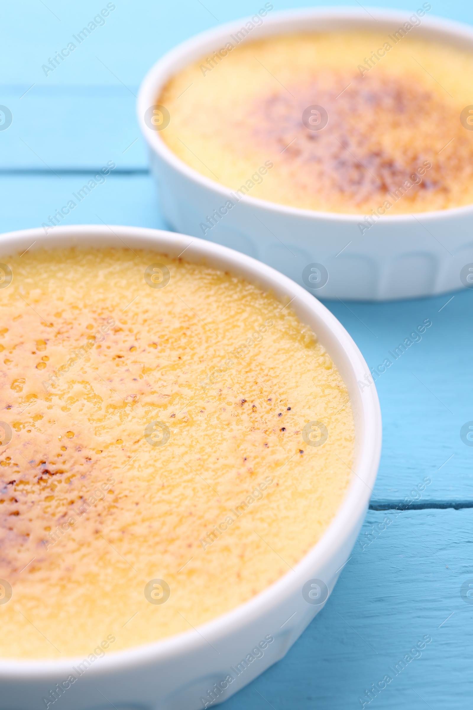 Photo of Delicious creme brulee in bowls on light blue wooden table, closeup