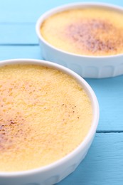 Photo of Delicious creme brulee in bowls on light blue wooden table, closeup
