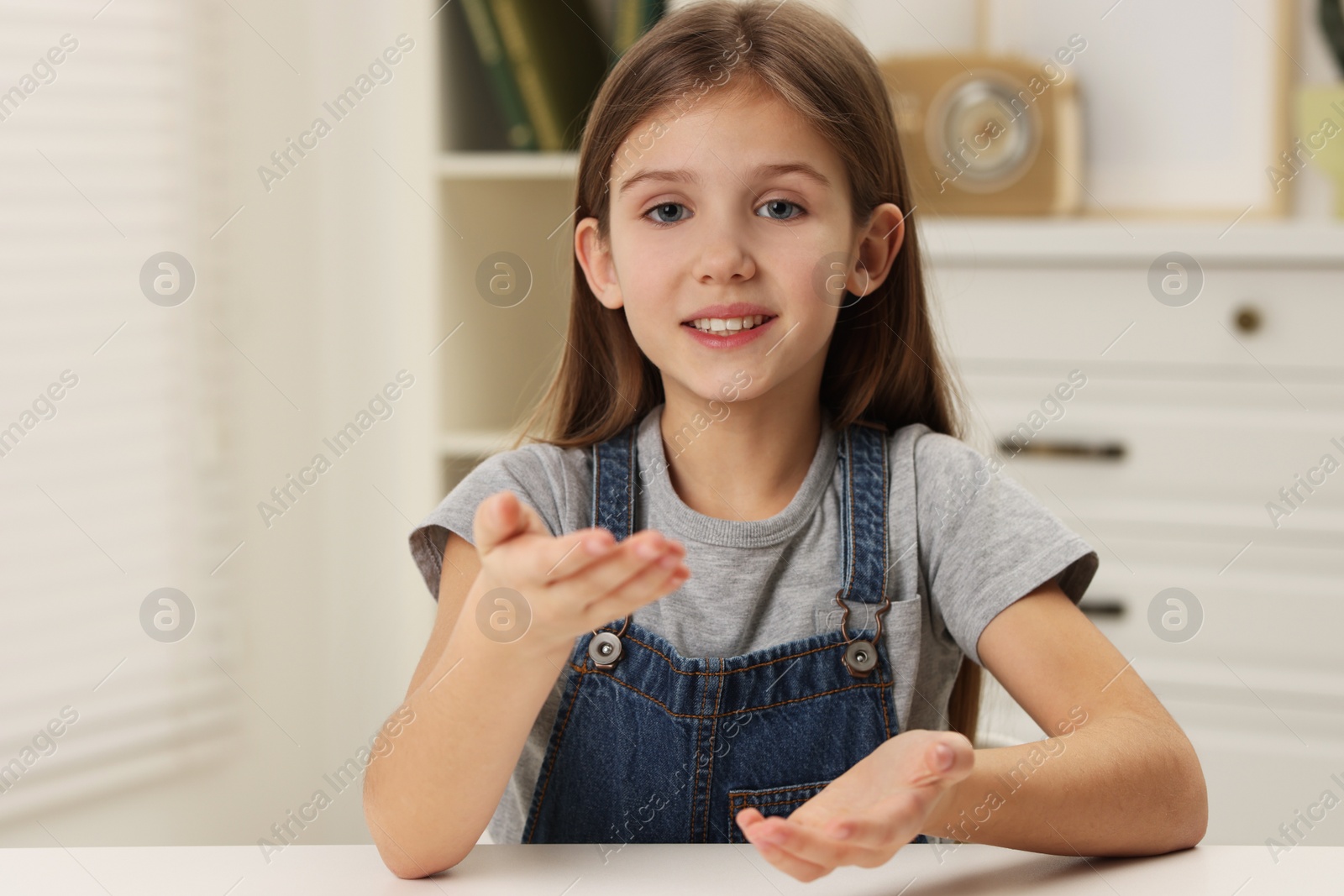 Photo of Cute little girl at white table indoors