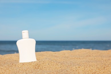 Blank white bottle of sunscreen on sand near sea, space for text
