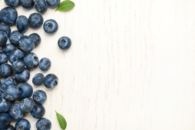 Photo of Fresh ripe blueberries on white wooden table, flat lay. Space for text