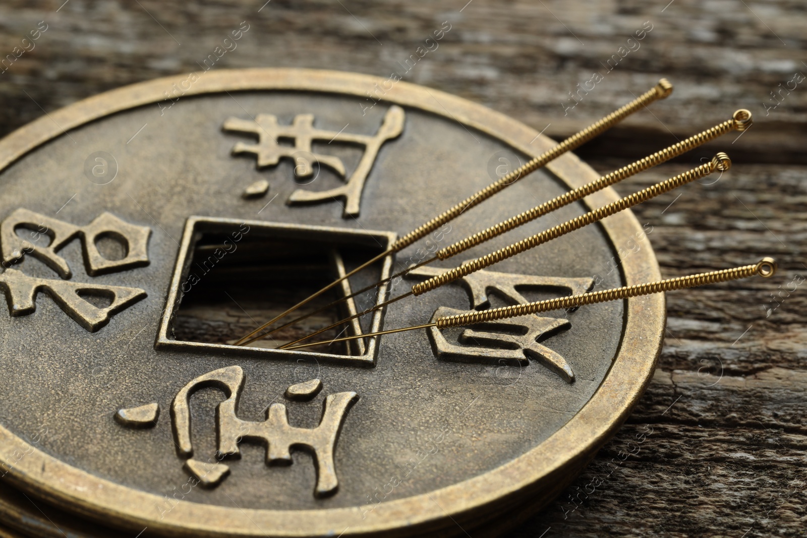 Photo of Acupuncture needles and stacked Chinese coins on wooden table, closeup