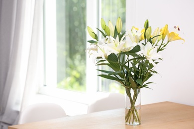 Vase with bouquet of beautiful lilies on wooden table indoors. Space for text