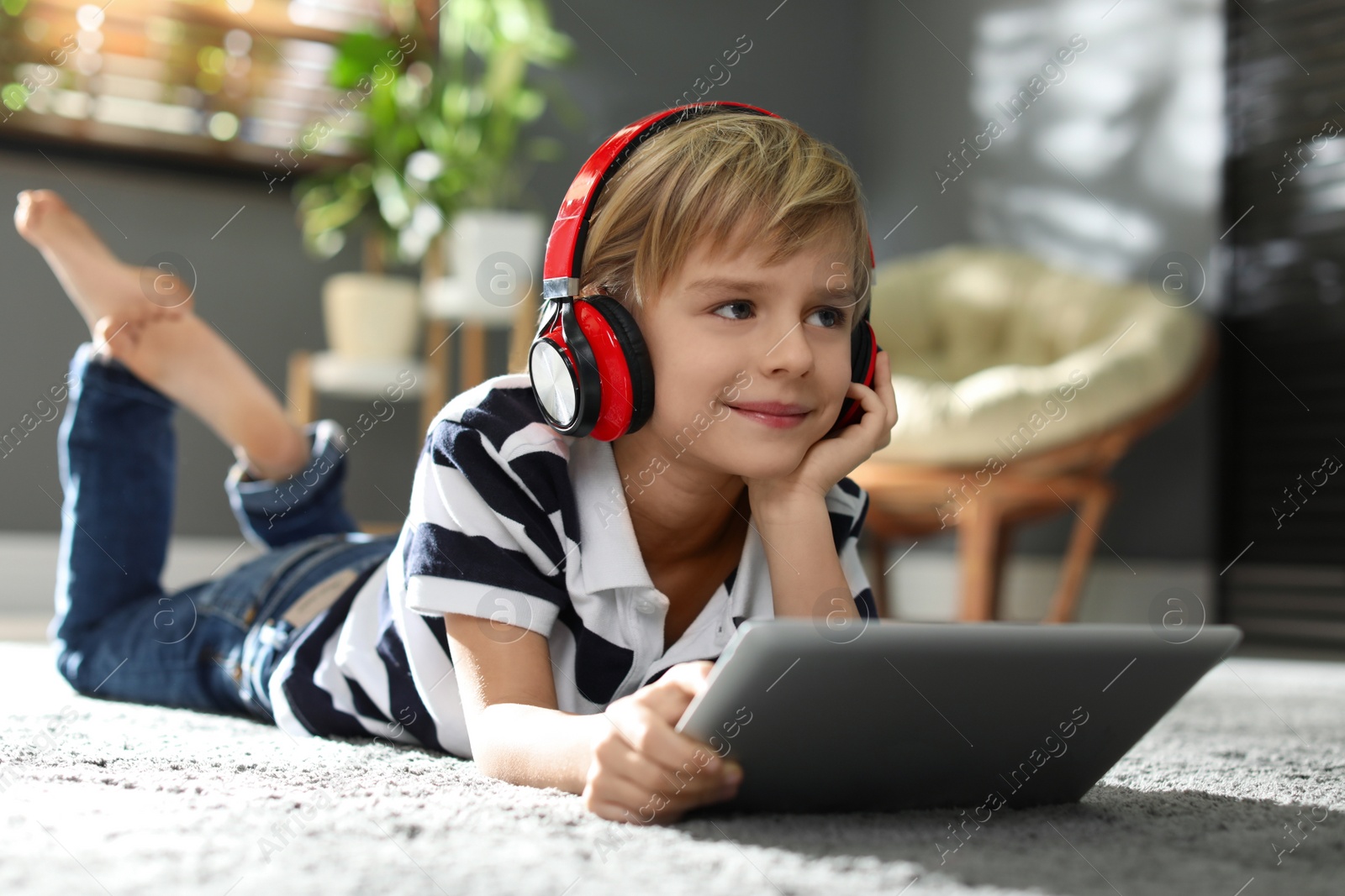 Photo of Cute little boy with headphones and tablet listening to audiobook at home