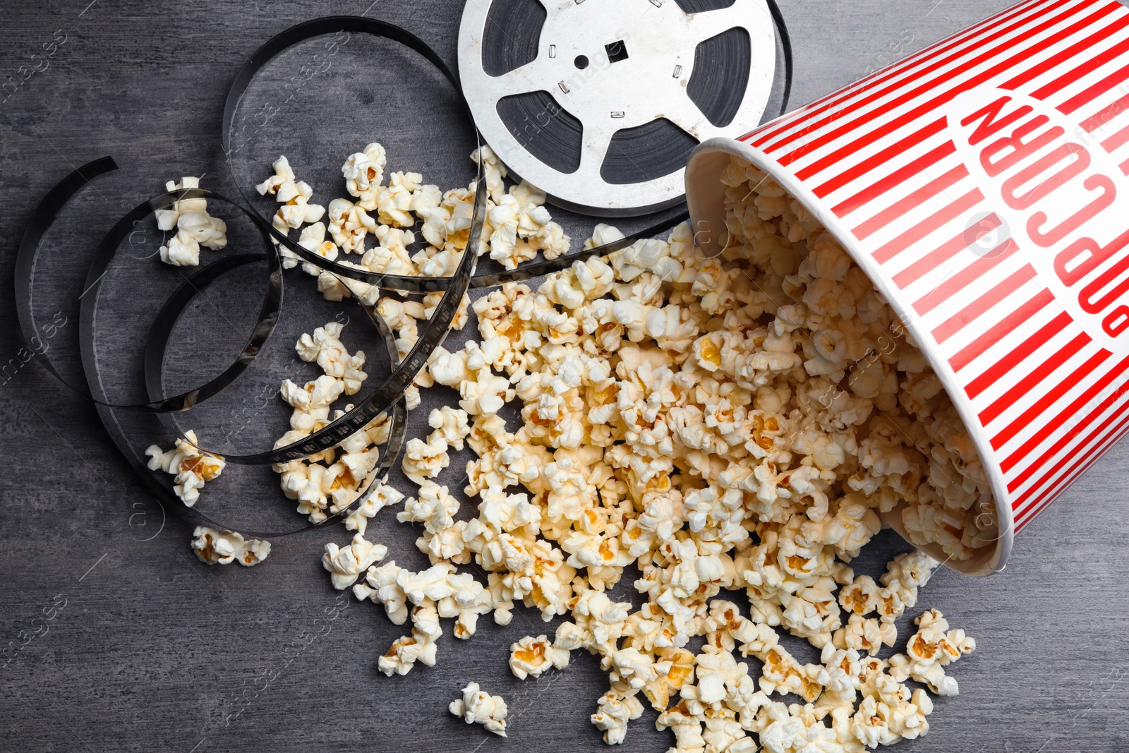 Photo of Popcorn and movie reel on grey stone table, flat lay. Cinema snack