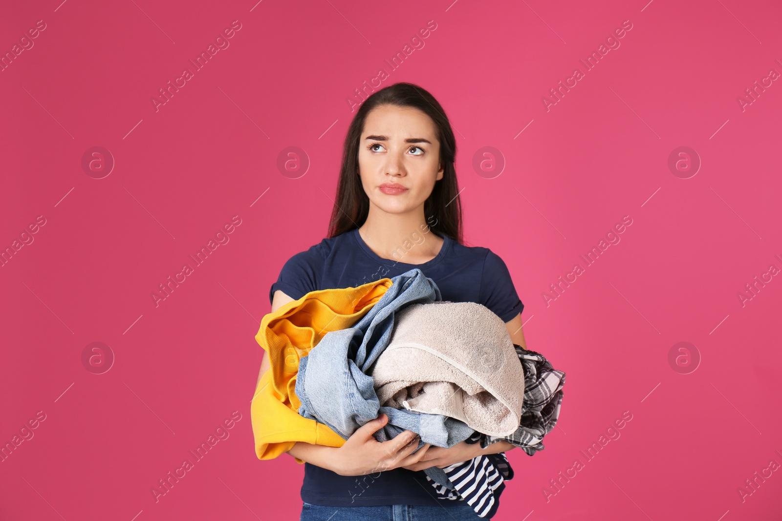 Photo of Displeased young woman holding pile of dirty laundry on color background