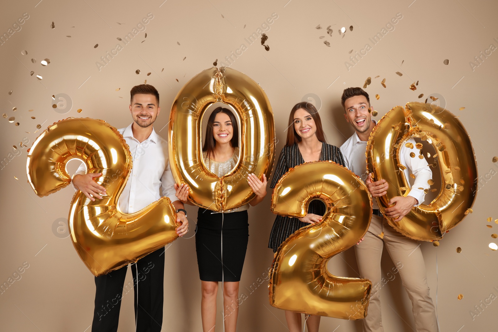 Photo of Happy young friends with golden 2020 balloons on beige background. New Year celebration