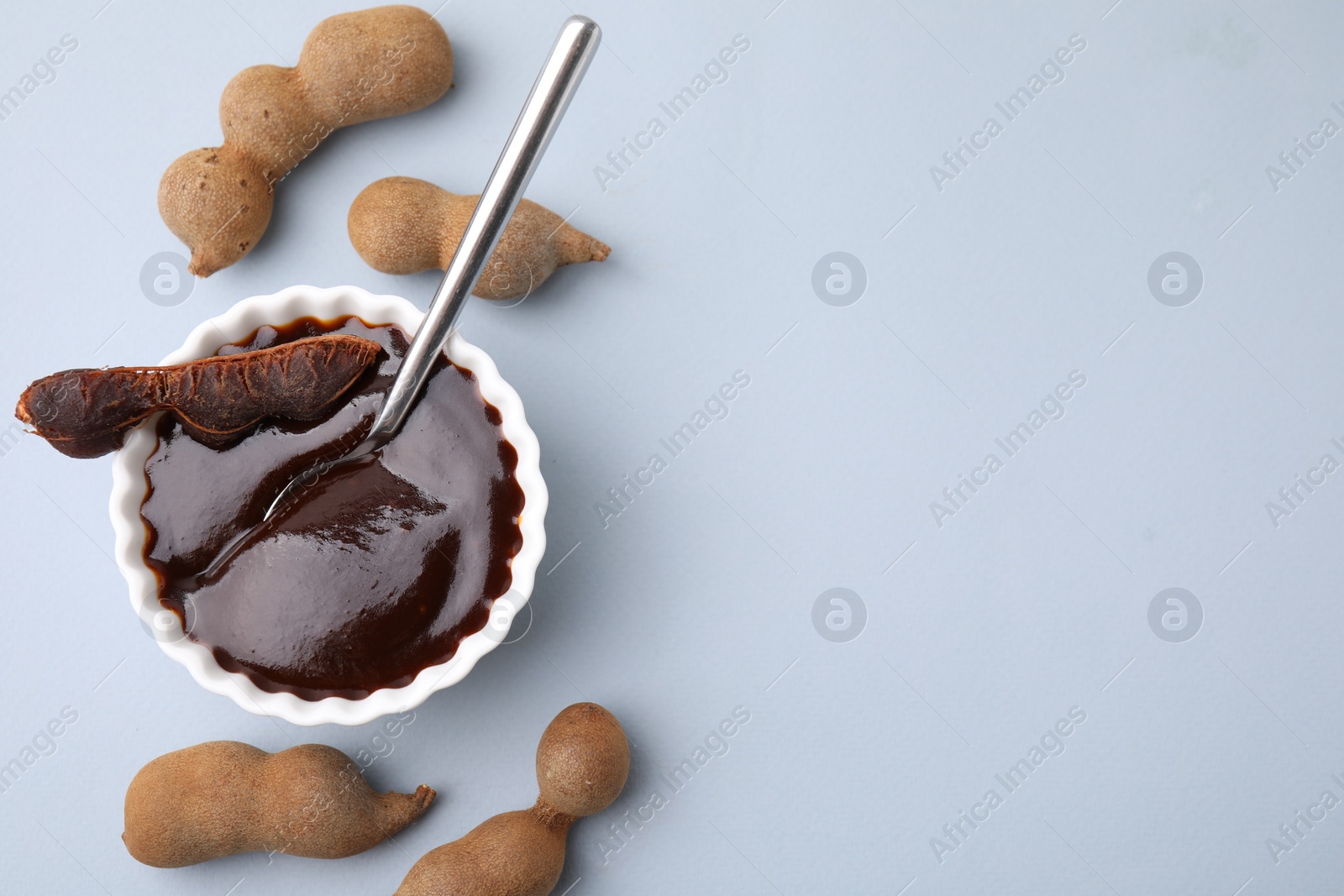 Bowl of tamarind sauce, spoon and fresh pods on light grey table, flat lay. Space for text Photo of Bowl of tamarind sauce, spoon and fresh pods on light grey table, flat lay. Space for text