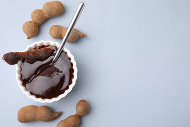 Photo of Bowl of tamarind sauce, spoon and fresh pods on light grey table, flat lay. Space for text