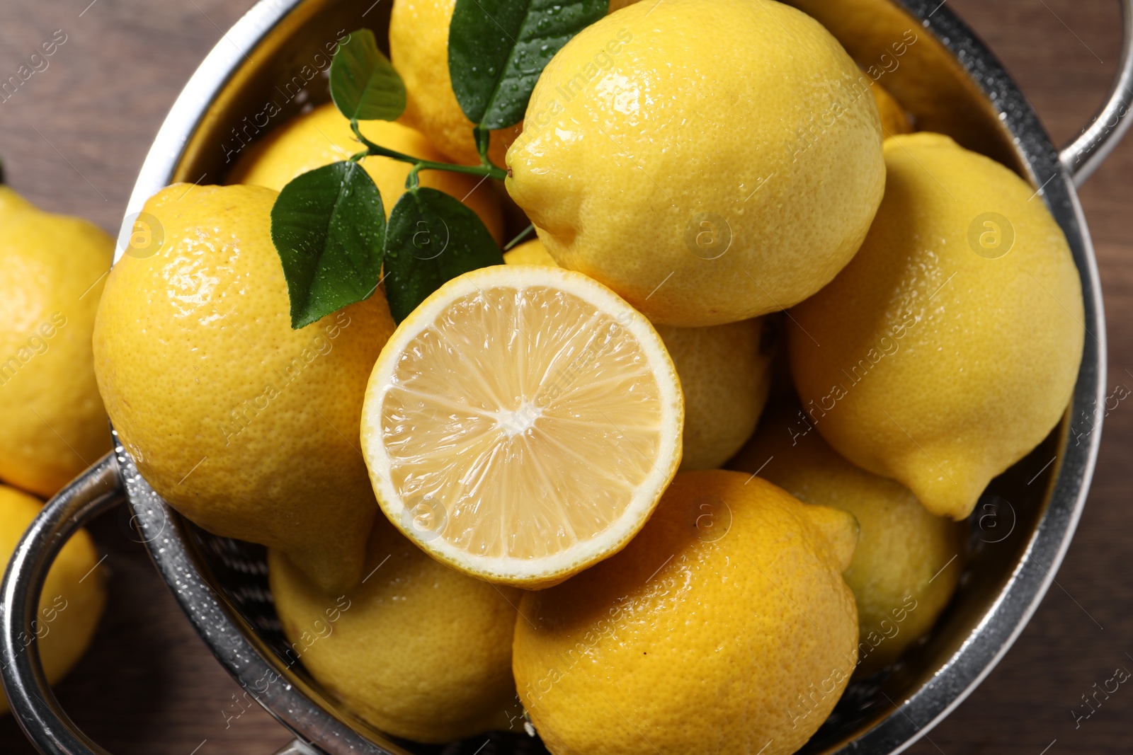 Photo of Fresh lemons and green leaves in colander on table, top view