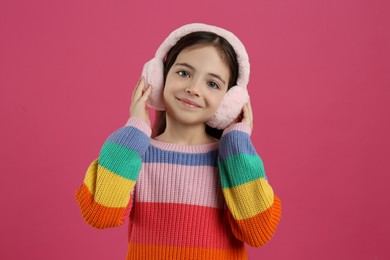 Photo of Cute little girl wearing stylish earmuffs on pink background