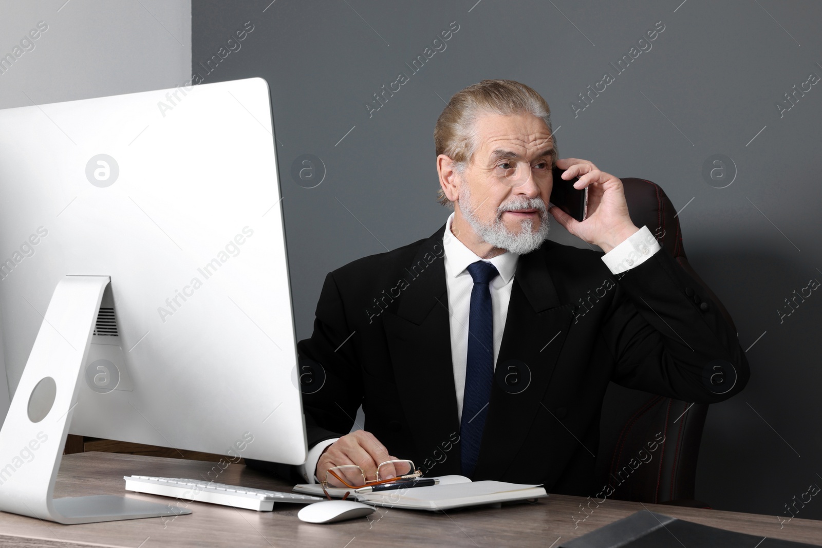 Photo of Senior boss talking on phone at wooden table in modern office