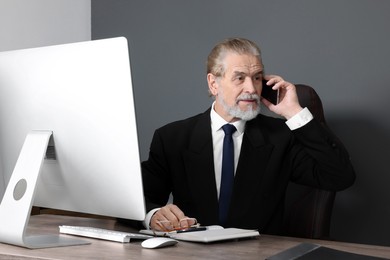 Photo of Senior boss talking on phone at wooden table in modern office