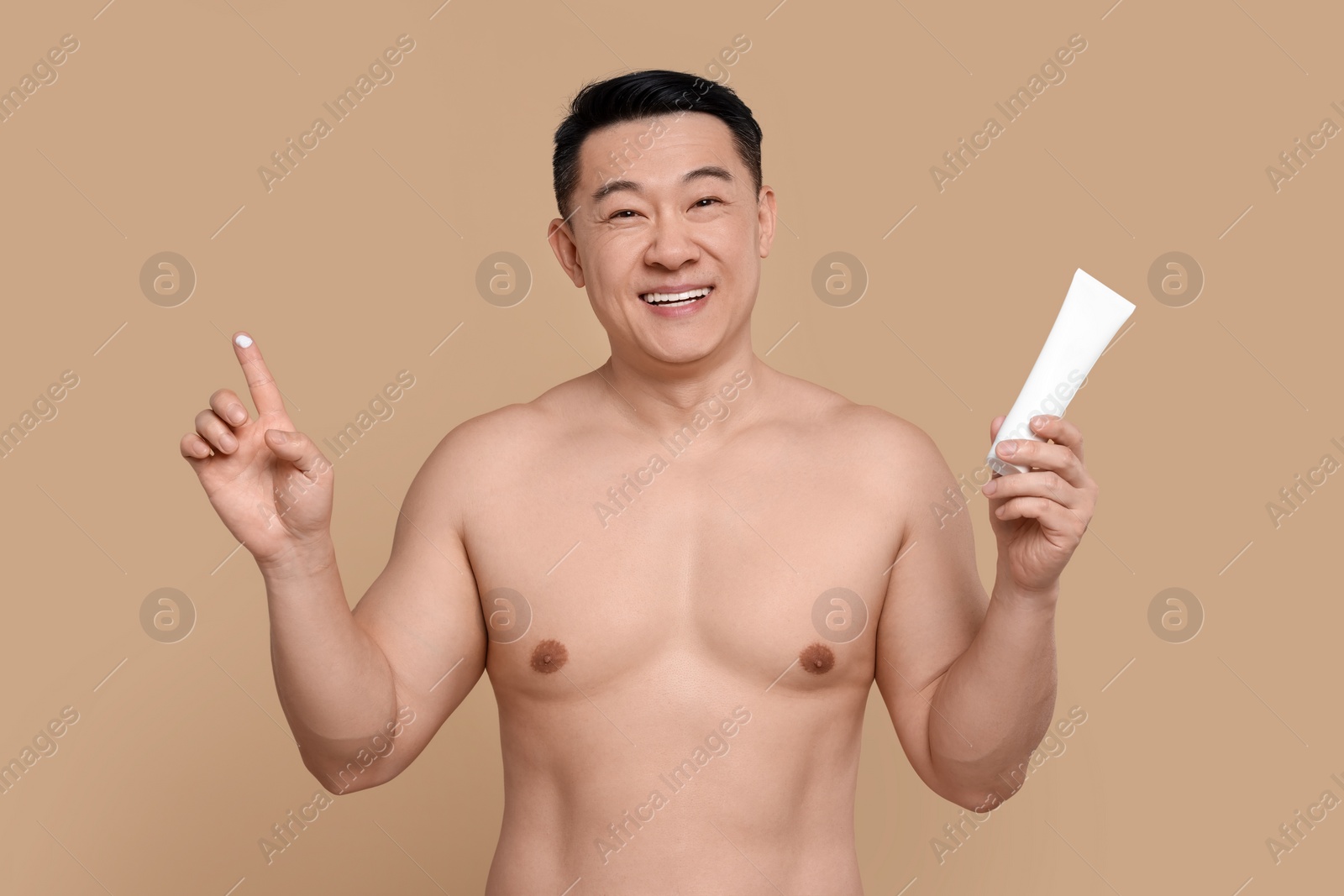 Photo of Handsome man with tube of body cream on light brown background