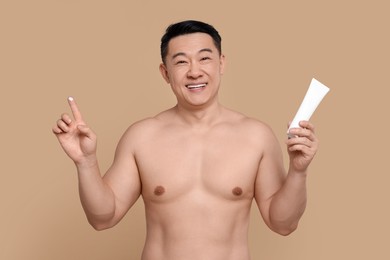 Photo of Handsome man with tube of body cream on light brown background