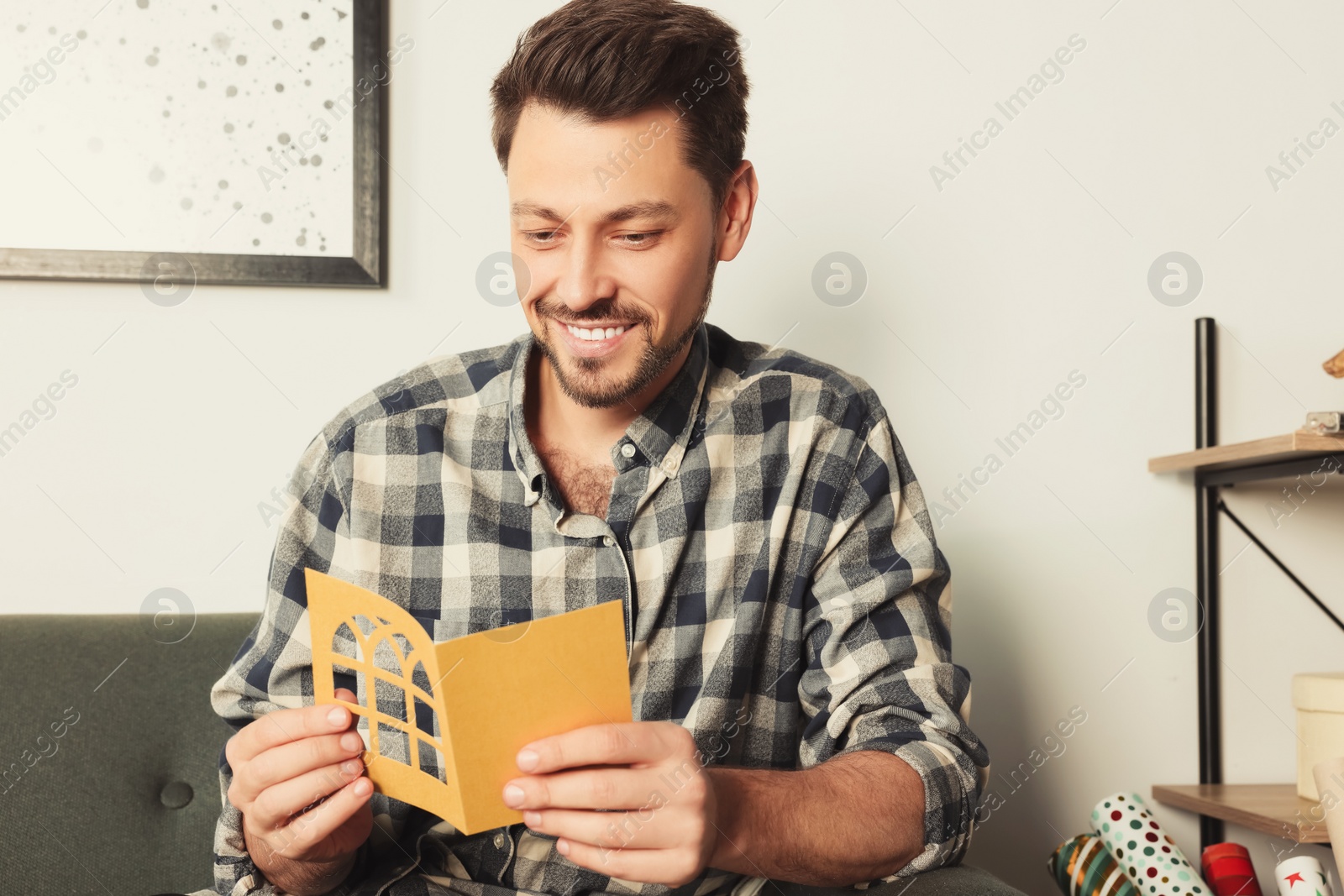 Photo of Happy man reading greeting card on sofa in living room