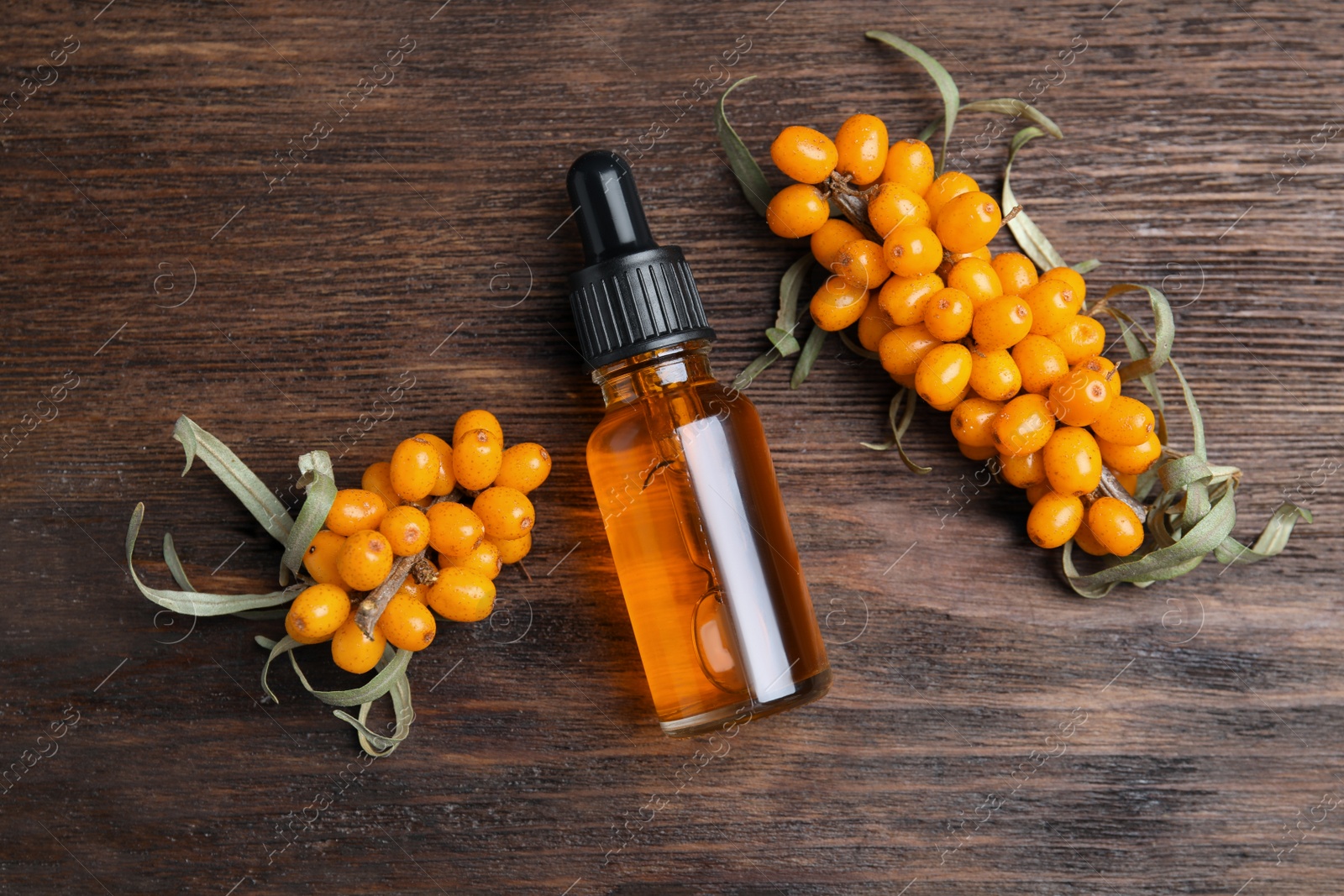 Photo of Ripe sea buckthorn and bottle of essential oil on wooden table, flat lay