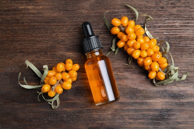 Photo of Ripe sea buckthorn and bottle of essential oil on wooden table, flat lay