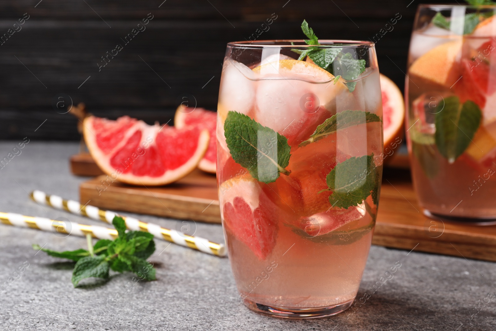 Photo of Glass of refreshing drink with grapefruit and mint on grey stone table against dark background, space for text