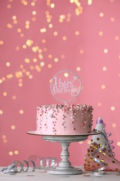 Photo of Beautiful birthday cake and decor on white table against blurred festive lights