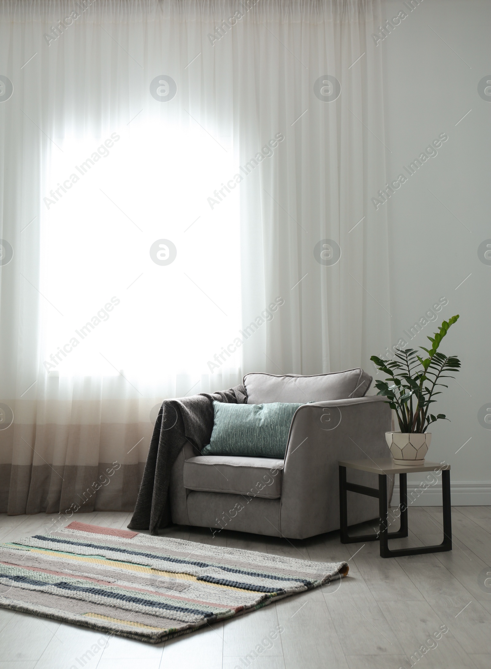 Photo of Cozy armchair with pillows and plaid near window in room. Interior design