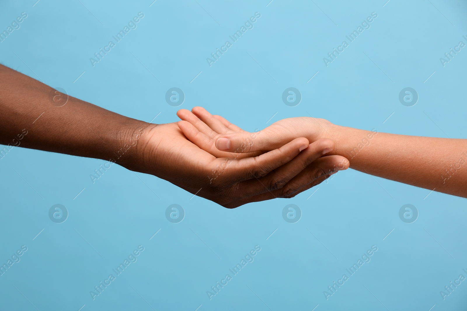 Photo of Woman and African American man holding hands on light blue background, closeup