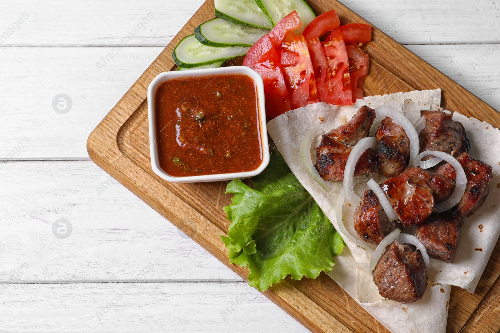 Photo of Wooden board with shish kebab and sauce on table, top view