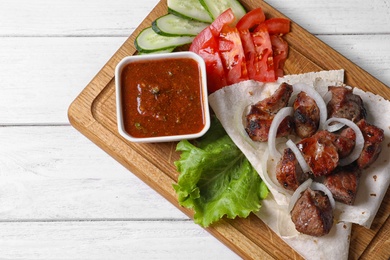 Photo of Wooden board with shish kebab and sauce on table, top view