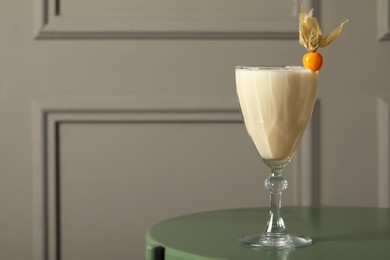 Photo of Refreshing cocktail decorated with physalis fruit on green table indoors. Space for text