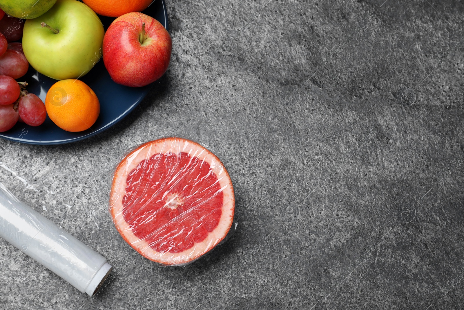 Photo of Fresh fruits and plastic food wrap on grey table, flat lay. Space for text