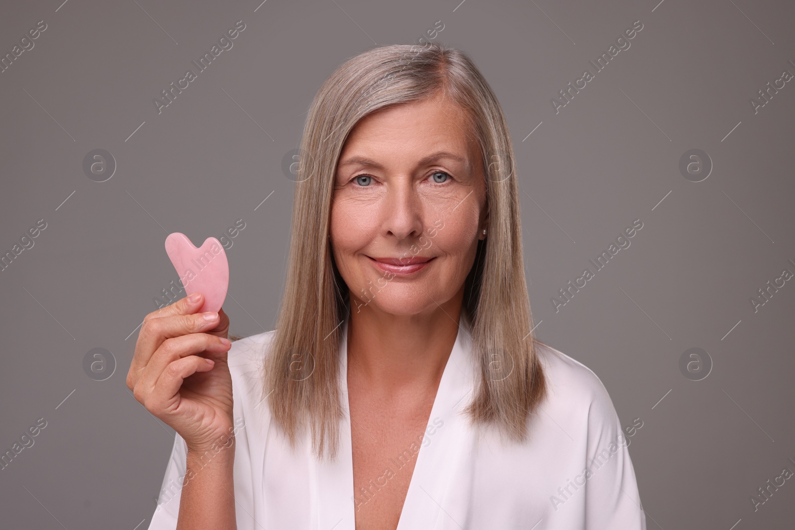 Photo of Woman with rose quartz gua sha tool on grey background. Facial massage