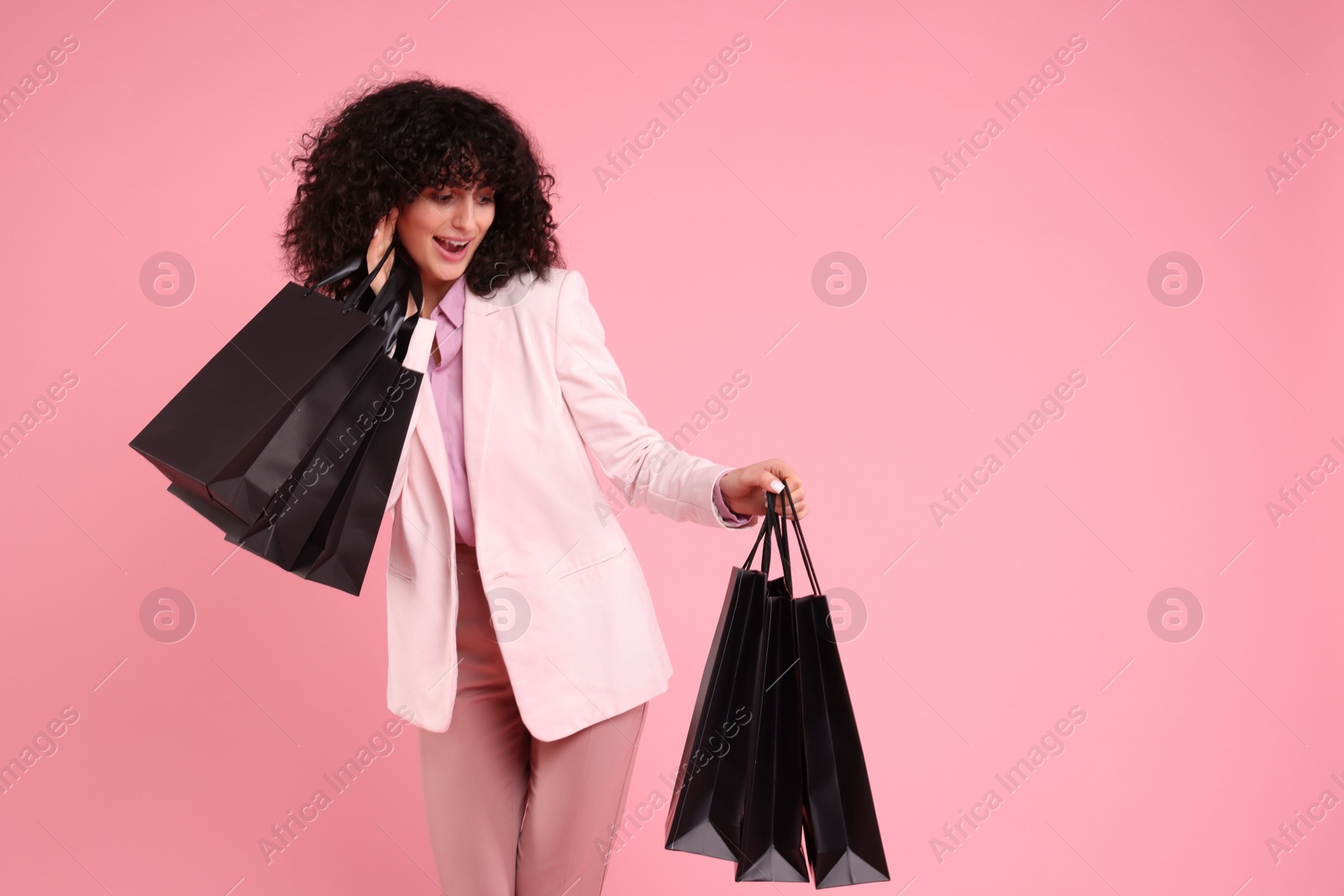 Photo of Happy young woman with shopping bags on pink background. Space for text