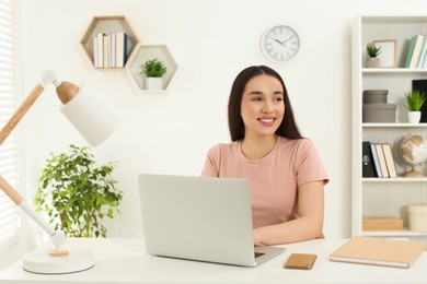 Home workplace. Woman working on laptop at white desk in room