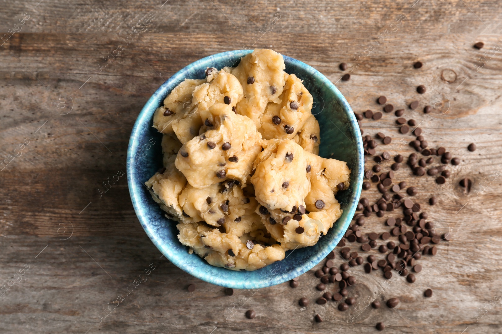 Photo of Raw cookie dough with chocolate chips in bowl on wooden background, top view